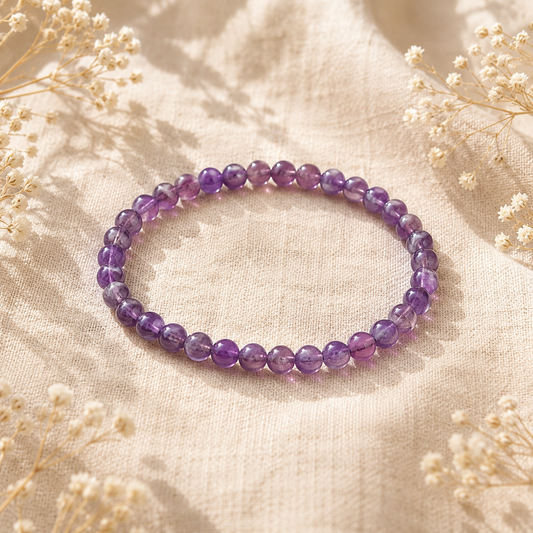 Bracelet en Améthyste naturelle posé sur un tissu en lin beige, entouré de fleurs séchées dans une ambiance chaleureuse.