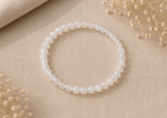 Bracelet en pierre de lune naturel posé sur un fond en lin beige, entouré de quelques fleurs séchées dans une ambiance douce et lumineuse.