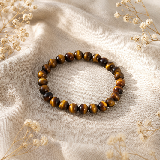 Bracelet en œil de tigre naturel posé sur un fond en lin beige, avec des reflets dorés et quelques fleurs séchées.
