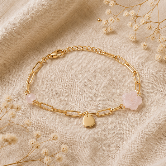 Bracelet à maillons dorés avec quartz rose et charme, posé sur un fond en lin beige entouré de fleurs séchées