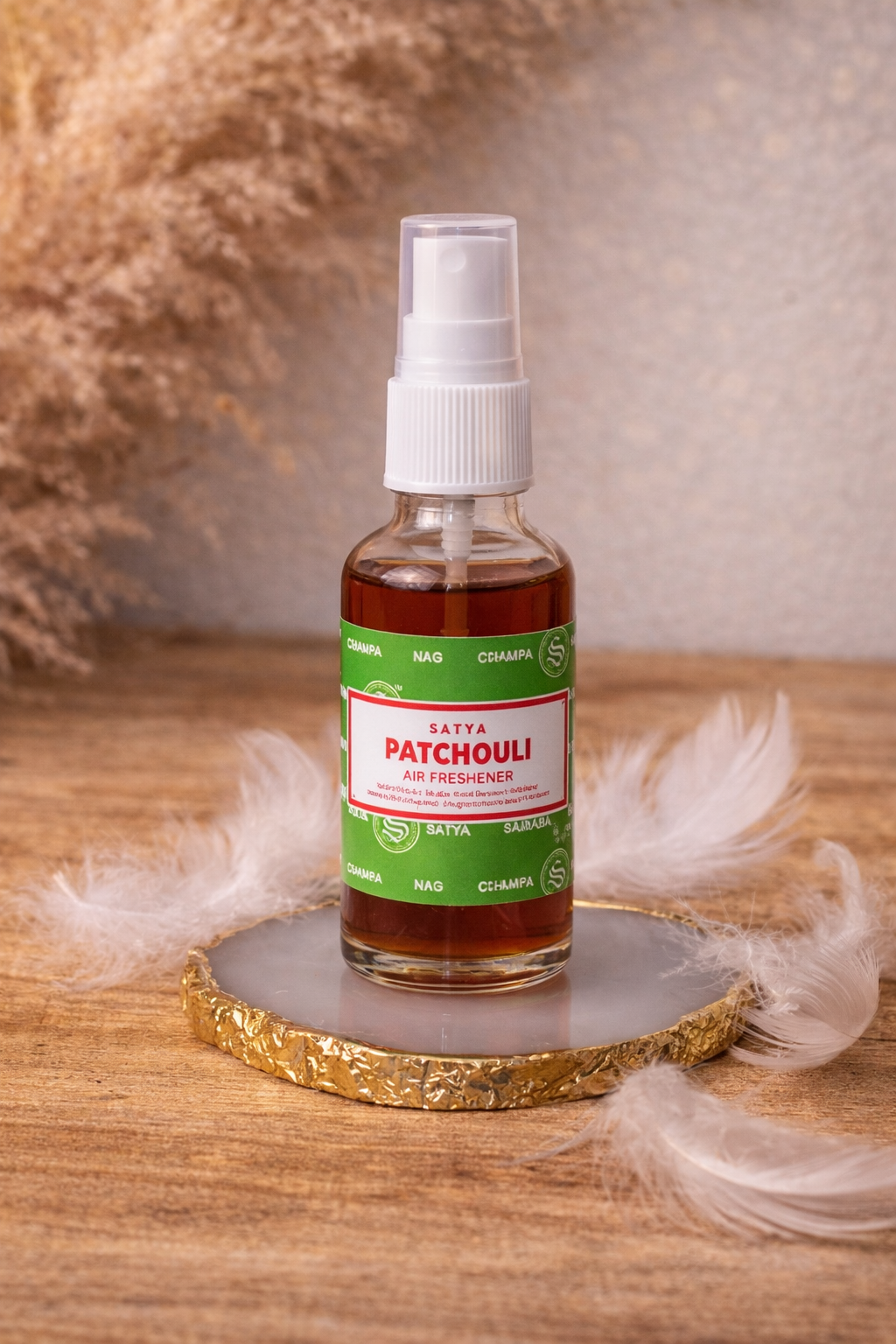 Spray parfumé Satya Patchouli posé sur une tranche d’agate blanche bordée d’or, décoré de plumes blanches dans une ambiance douce et spirituelle.