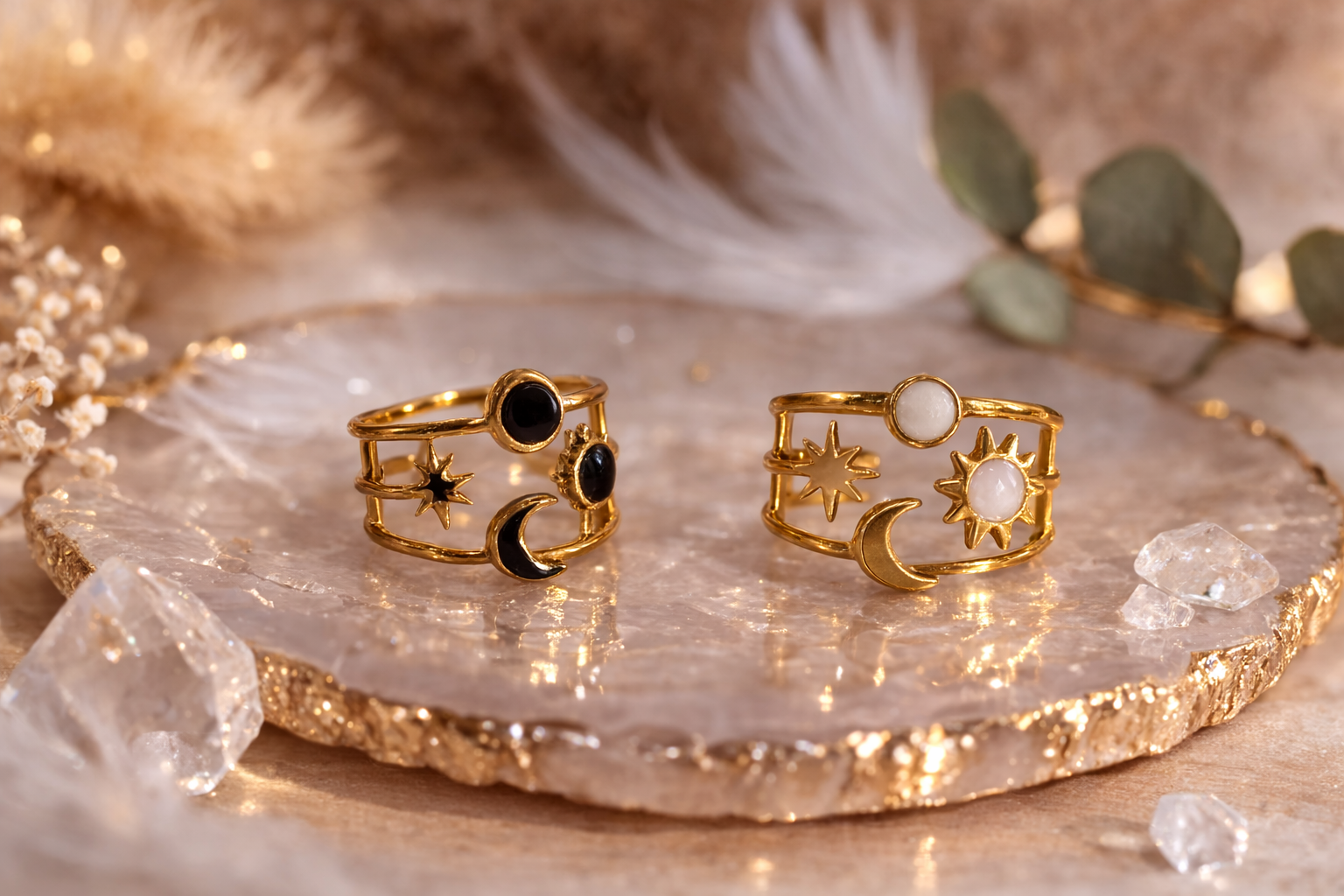 Bague ajustable plaquée or avec motif soleil et lune, ornée d’une pierre noire ou blanche, posée sur une coupelle en pierre avec décor naturel et plumes en arrière-plan