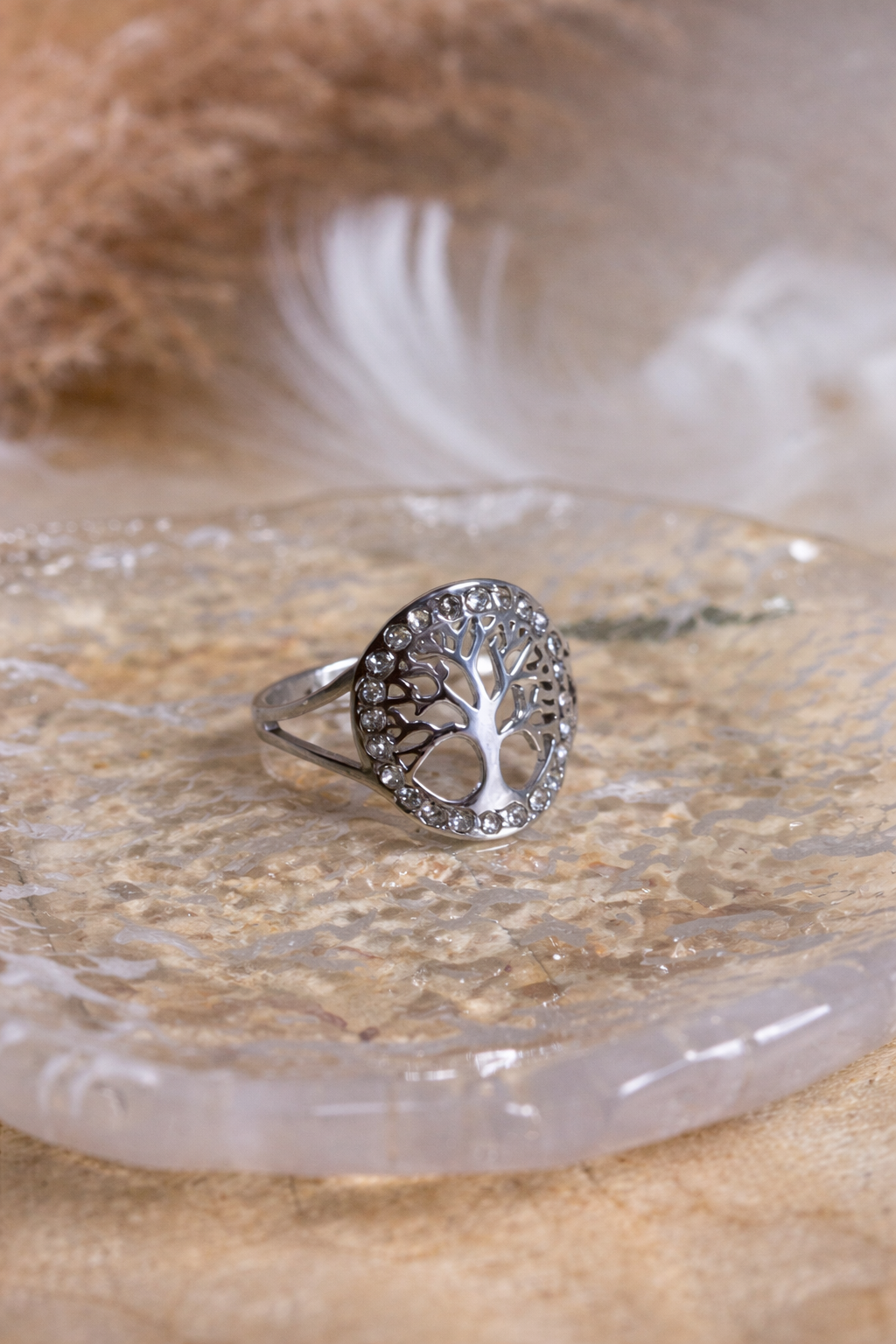 Bague arbre de vie en acier inoxydable sertie de cristaux, présentée sur une tranche d’agate dans une ambiance douce et spirituelle.