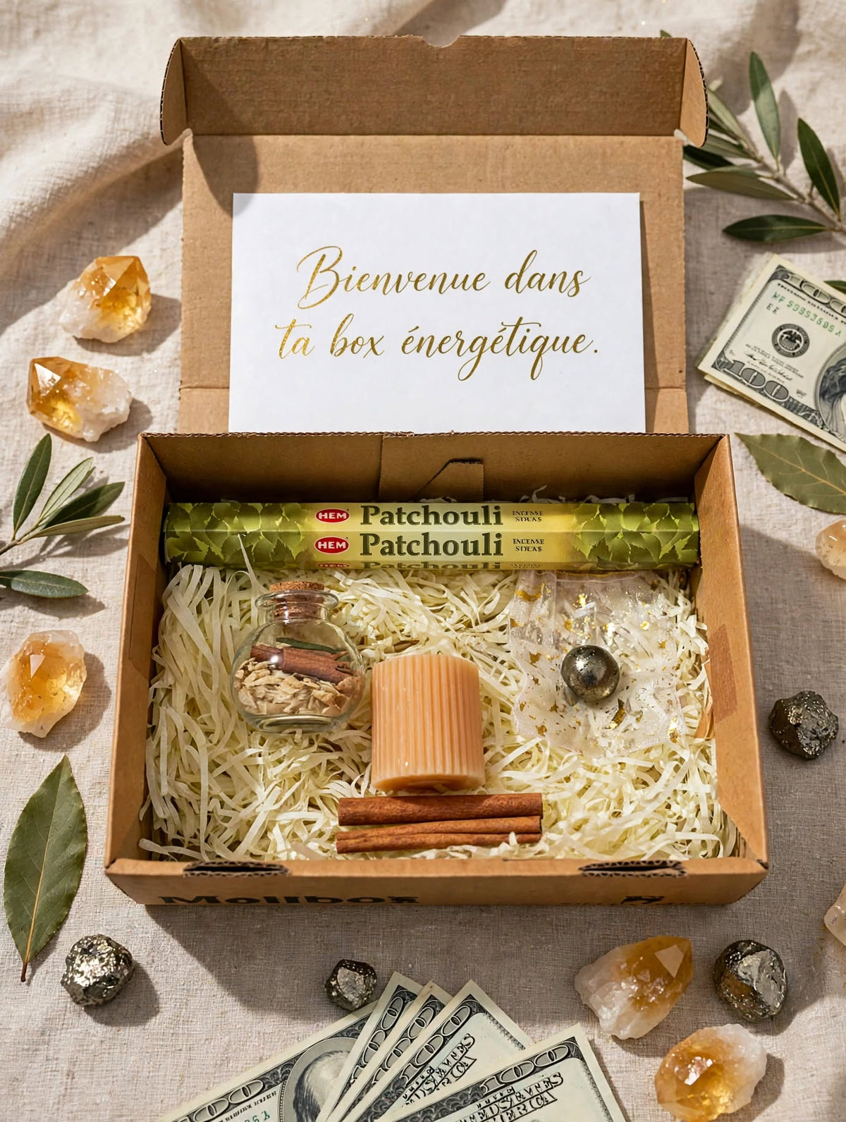 Box abondance ouverte avec encens HEM Patchouli, spell jar abondance cannelle et herbes, bougie pilier pêche cannelée, sphère pyrite, bâtons de cannelle sur frisure kraft
