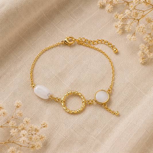 Bracelet doré orné de quartz rose et d’un anneau torsadé, posé sur un tissu en lin beige avec des fleurs séchées.