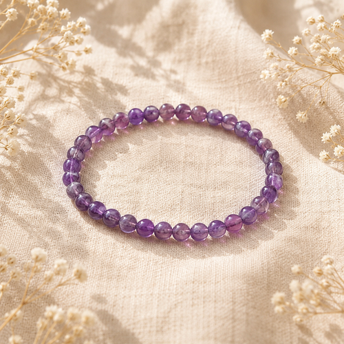 Bracelet en Améthyste naturelle posé sur un tissu en lin beige, entouré de fleurs séchées dans une ambiance chaleureuse.