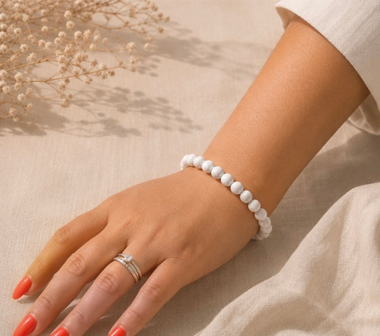 Bracelet en howlite blanche naturelle porté sur un fond en lin beige, entouré de fleurs séchées dans une ambiance lumineuse et épurée.