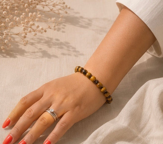 
Bracelet en œil de tigre naturel porté sur un fond en lin beige, avec des reflets dorés et quelques fleurs séchées.