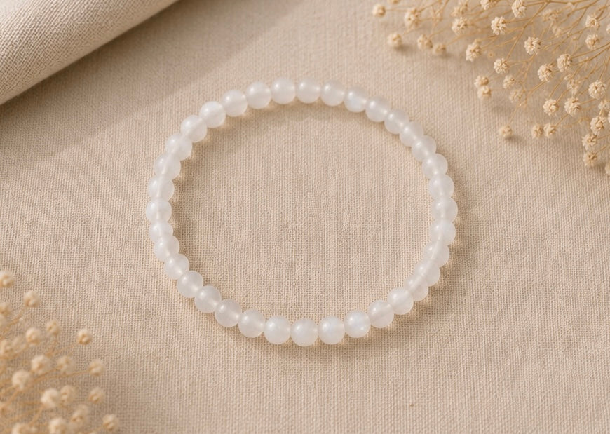 
Bracelet en pierre de lune naturel posé sur un fond en lin beige, entouré de quelques fleurs séchées dans une ambiance douce et lumineuse.