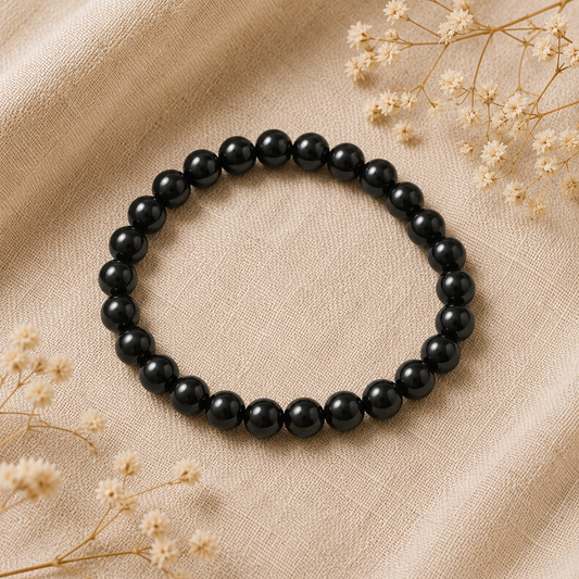 Bracelet en obsidienne noire naturelle posé sur un tissu en lin beige, entouré de fleurs séchées dans une ambiance élégante et épurée.