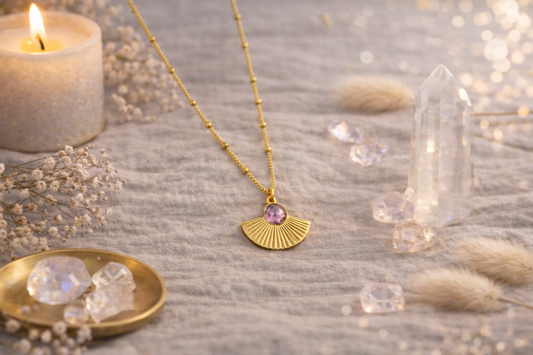 Collier doré avec pendentif éventail et pierre violette porté autour du cou d’une femme, bijou élégant et lumineux.