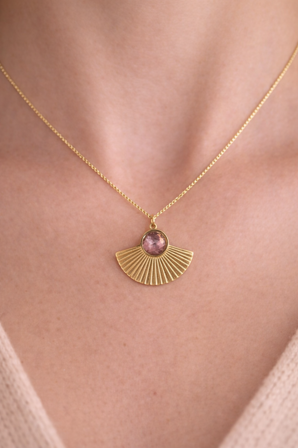 Collier doré porté autour du cou avec pendentif en forme de rayon de lumière et pierre violette, bijou fin et élégant. 