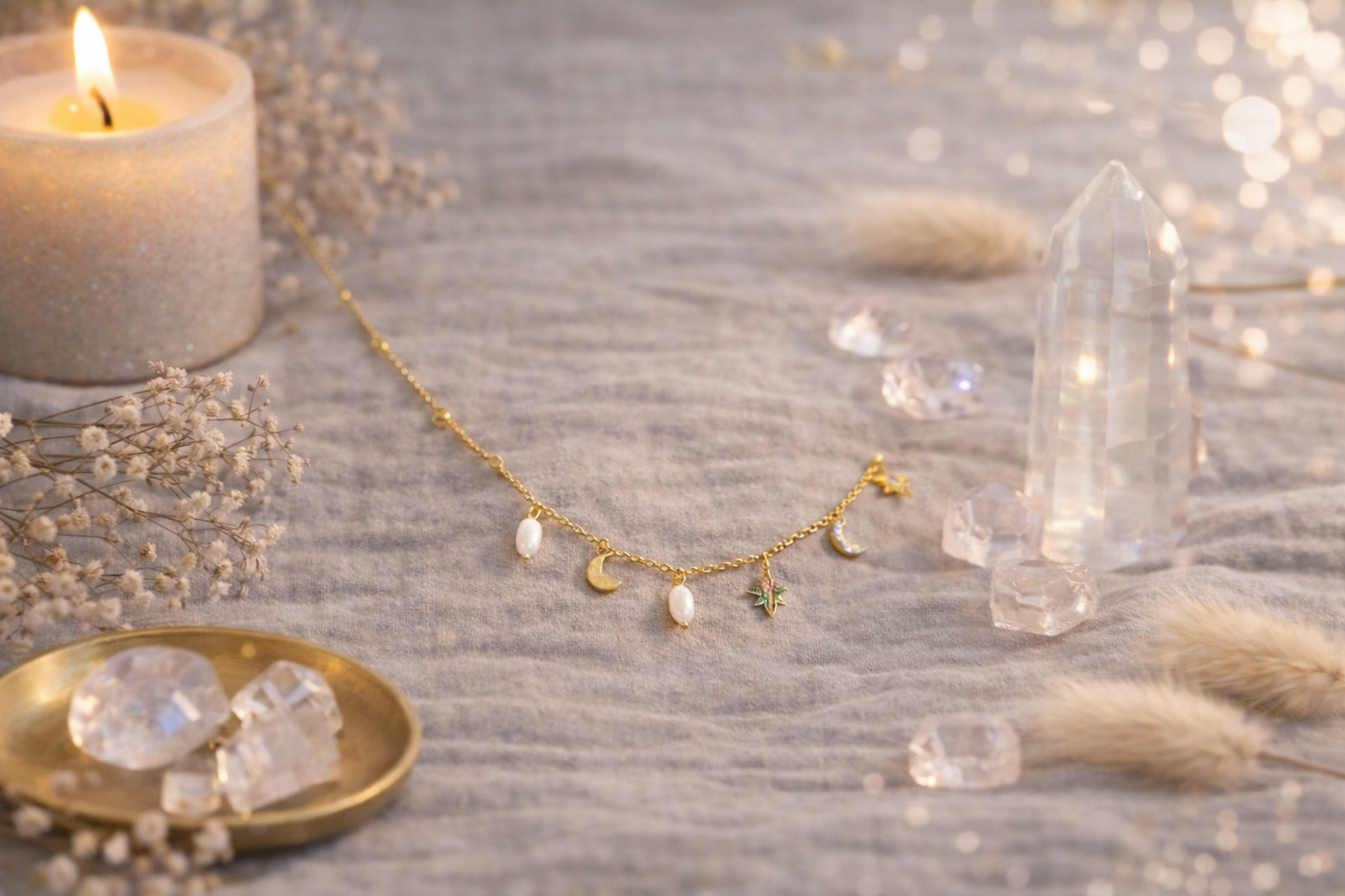 Collier plaqué or 18k en acier inoxydable avec pendentifs lune, étoile et perles, posé sur un décor doux avec bougie et cristaux. 