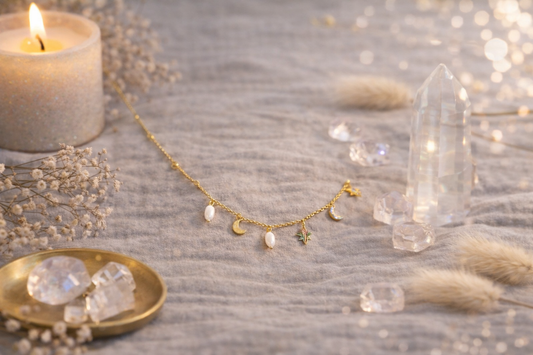 Collier plaqué or 18k en acier inoxydable avec pendentifs lune, étoile et perles, posé sur un décor doux avec bougie et cristaux. 