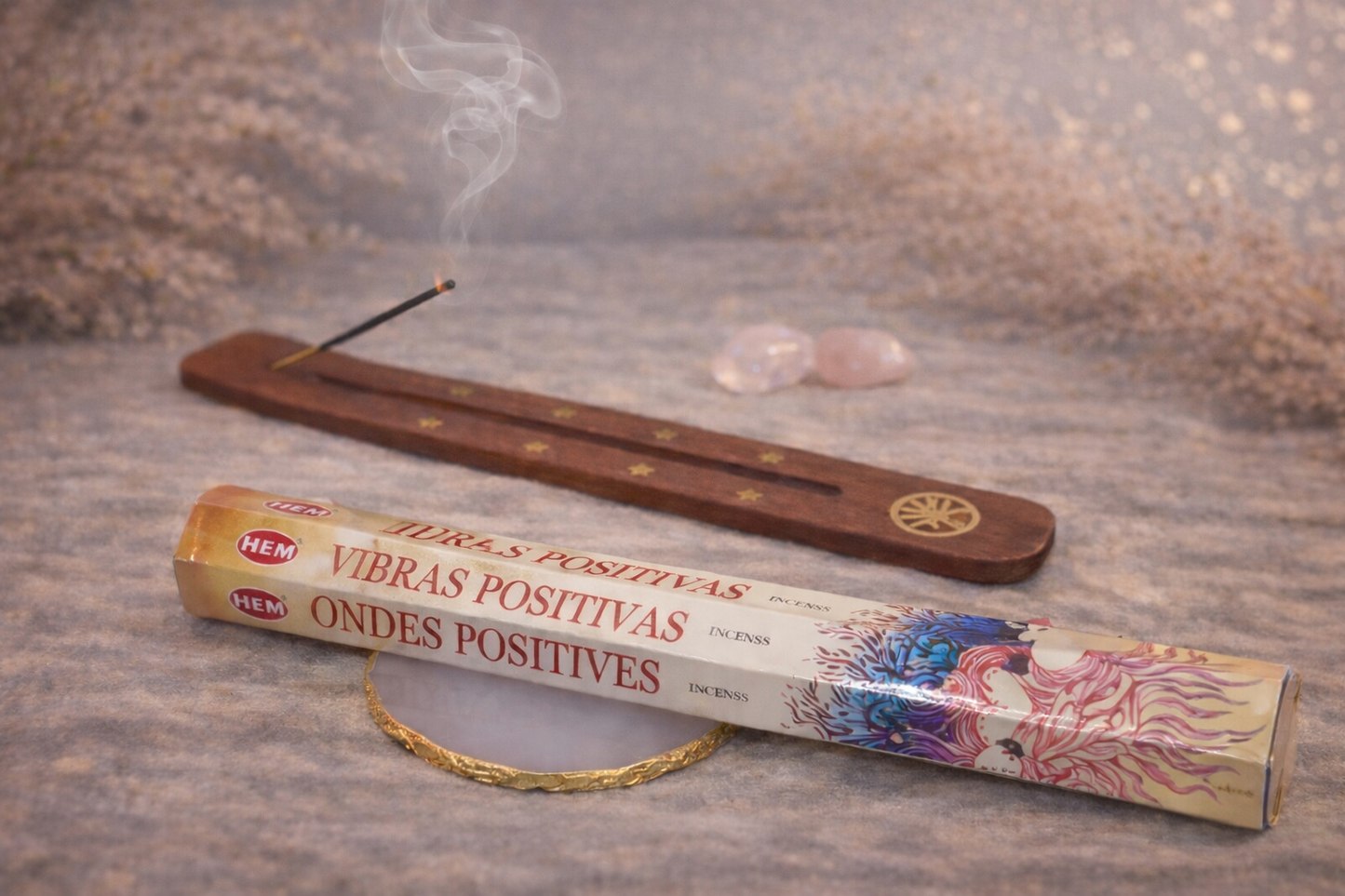 Encens HEM Ondes Positives présenté dans une ambiance zen avec porte-encens en bois, fumée d’encens et pierres naturelles sur table en bois.