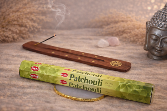 Encens HEM Patchouli présenté dans une ambiance zen avec porte-encens en bois, statuette Bouddha, fumée d’encens et pierres naturelles sur table en bois