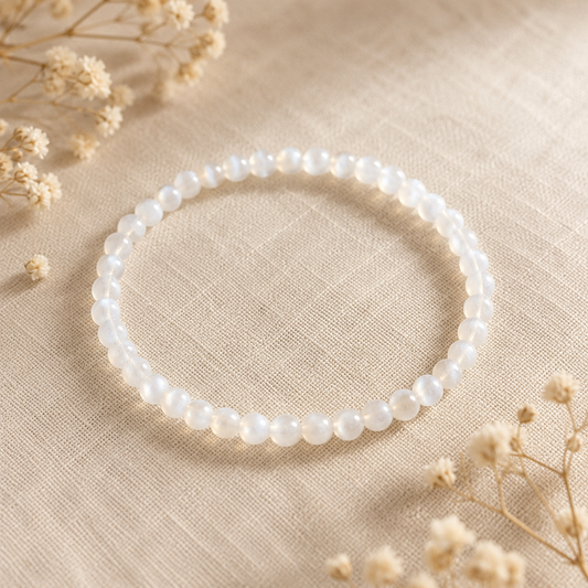 Bracelet en Pierre de Lune naturelle posé sur un tissu en lin beige, entouré de fleurs séchées dans une ambiance douce et lumineuse.