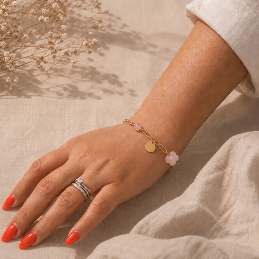 Main portant un bracelet à maillons dorés orné de quartz rose et d’un charme délicat, sur fond en lin beige.