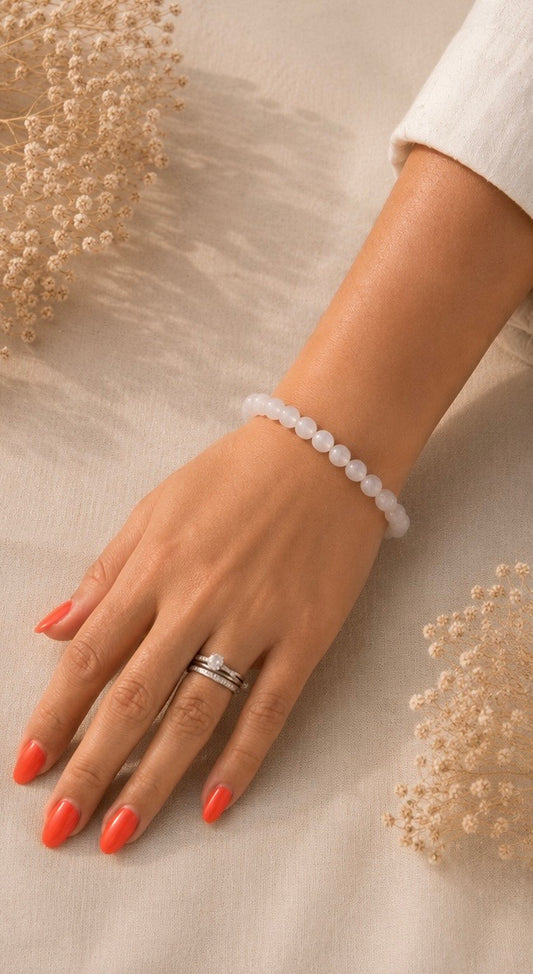 Main portant un bracelet pierre de lune naturel sur fond en lin beige, avec une lumière douce, une tenue claire et des fleurs séchées.